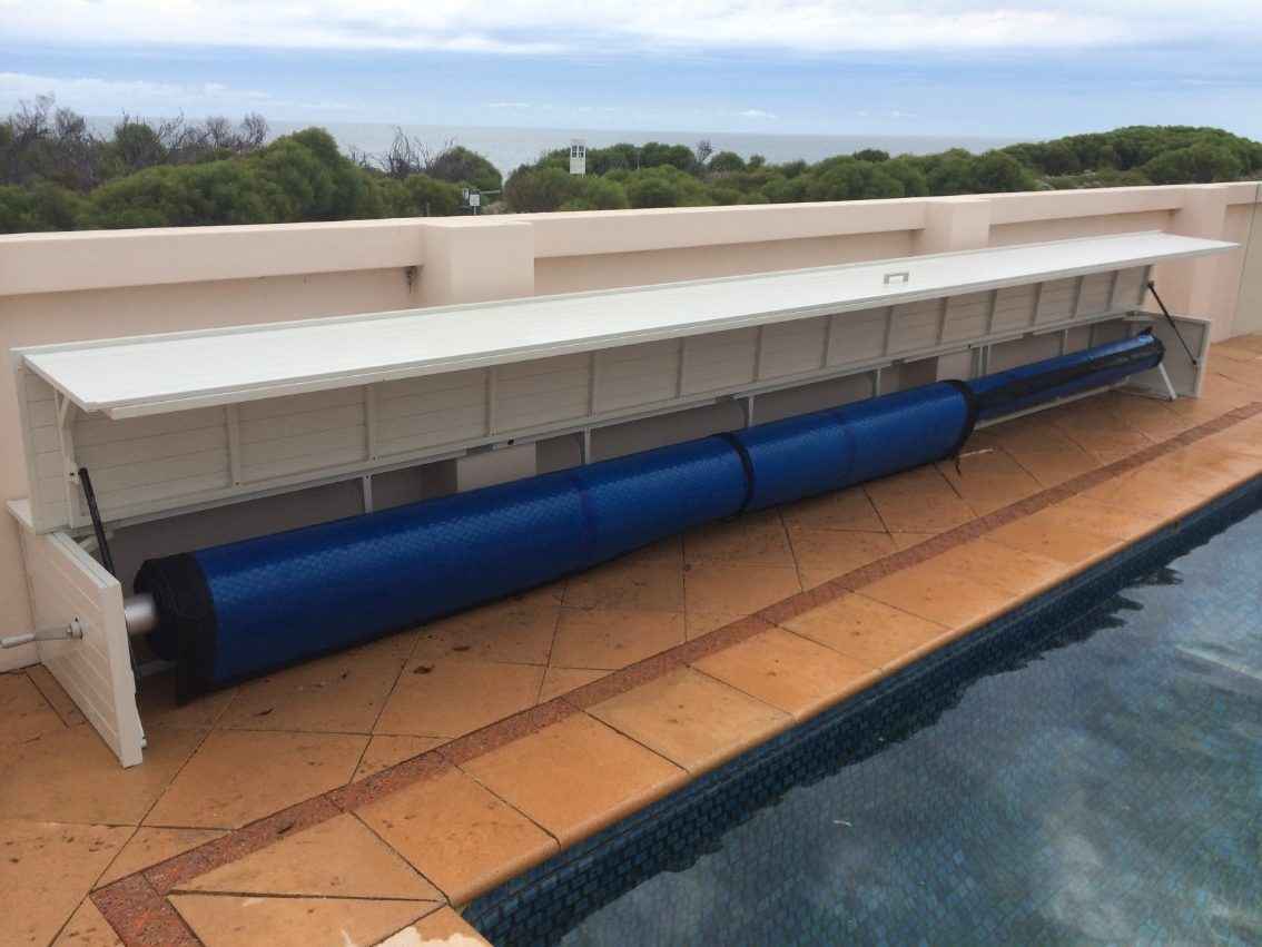 White pool roller and cover box with a dark blue pool cover